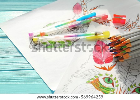 Colouring pictures, pencils and pens on wooden table, closeup
