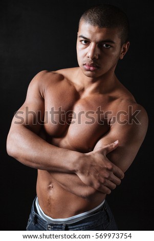 Picture of attractive young african sportsman standing over black background and looking at camera.