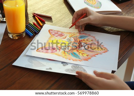 Young woman coloring pictures for adults on table