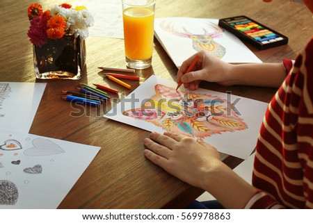 Young woman coloring pictures for adults on table