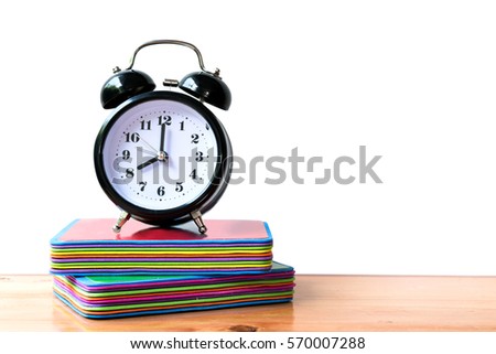 The alarm clock at 8.00 o'clock, black color, on top of Book cards for child,  on the wood table, white background