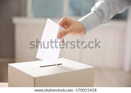 Closeup of hand inserting envelope in ballot box Royalty-Free Stock Photo #570015418