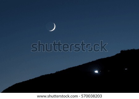 A night landscape: Moon is over the mountains and a car is coming  up in San Francisco, CA, USA.
