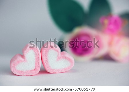 Heart shape marshmallow with blurred rose flower background.