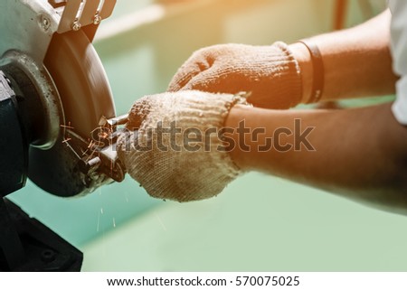 A worker is grinding a cutting tool with grinding stone for use in the turning machine. Royalty-Free Stock Photo #570075025