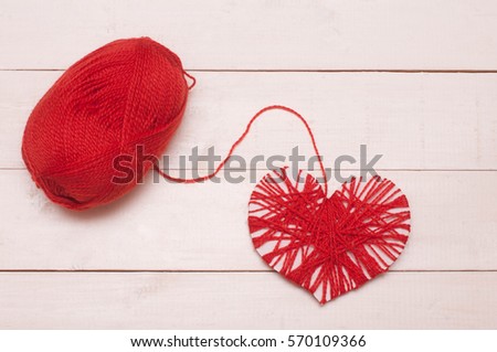Red heart shape symbol made from wool isolated on a wooden background