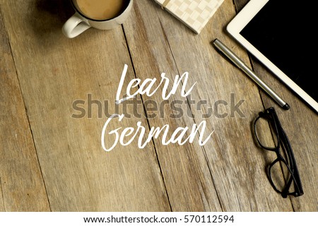 Education concept. Top view of tablet, glasses. notebook pen and a cup of coffee with LEARN GERMAN written on wooden background.