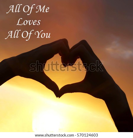 Hand heart shape silhouette made against the sun & sky of a sunrise or sunset with the romantic message of All Of Me Loves All Of You