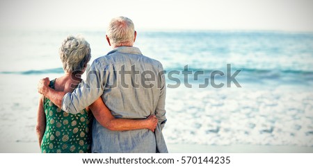Rear view of senior couple at beach against sea Royalty-Free Stock Photo #570144235