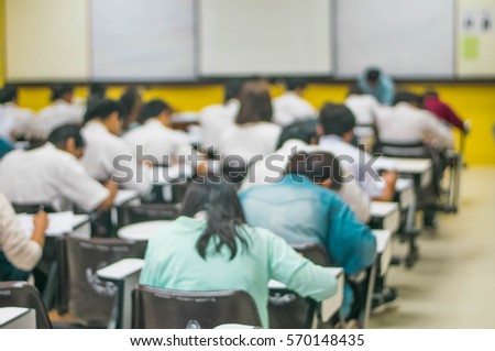 Blur abstract background of examination room with undergraduate students inside. Blurred view of student doing final test in exam hall. Blurry view of study chairs in classroom of university or campus Royalty-Free Stock Photo #570148435