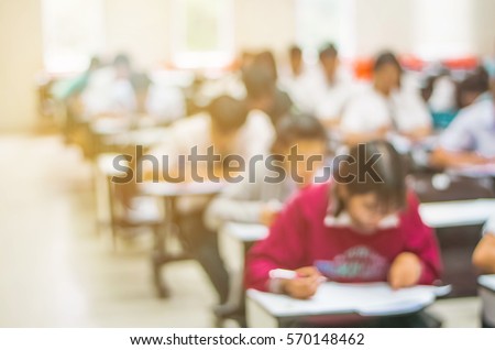 Blur abstract background of examination room with undergraduate students inside. Blurred view of student doing final test in exam hall. Blurry view of study chairs in classroom of university or campus Royalty-Free Stock Photo #570148462