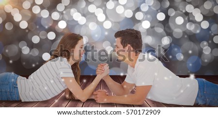 Happy couple arm wrestling against glowing background