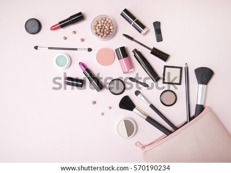 A pink makeup bag with cosmetic beauty products spilling out on to a pastel colored background, with empty space at side Royalty-Free Stock Photo #570190234