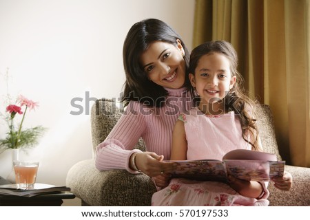 little girl sits on mother's lap, both smile at camera