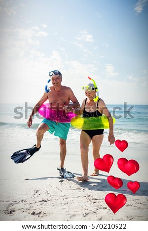 Floating love hearts against senior couple enjoying on beach 3d