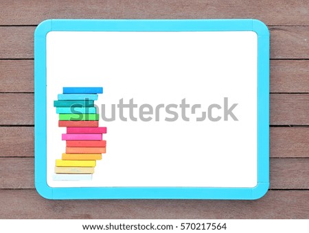 Blank white blackboard with colorful chalk on wooden plank.