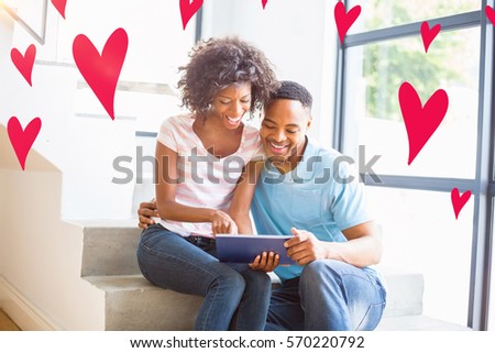 Red Hearts against happy couple using digital tablet at home
