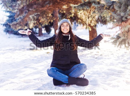 Cheerful smiling young woman sitting on snow in winter .Winter holidays concept