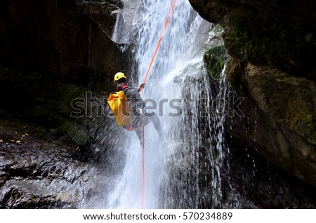 Man hanging of a rope at the bottom of a waterfall   Royalty-Free Stock Photo #570234889
