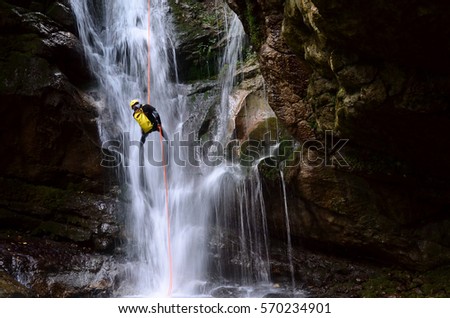 man rappelling down a waterfall with yellow backpack   Royalty-Free Stock Photo #570234901