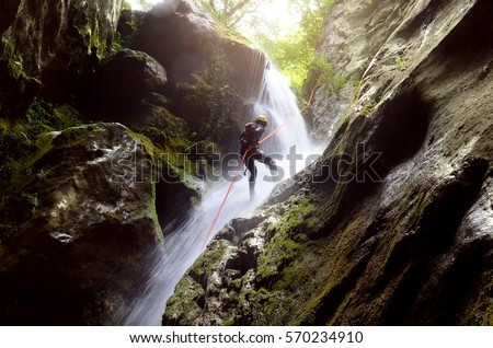 man rappelling down a waterfall backlit  Royalty-Free Stock Photo #570234910