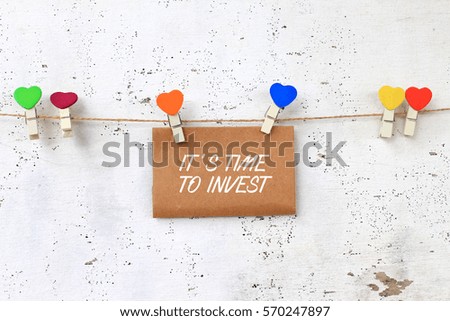 Business concept - words on paper writing IT'S TIME TO INVEST with wooden clamps on rustic wooden background.
