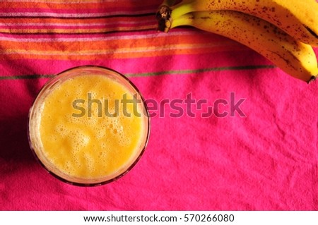 Healthy banana and mango smoothie on a vibrant pink, red and orange tea towel. Overripe bananas.