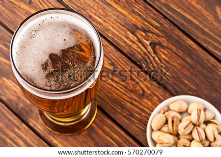 glass of dark cold frothy beer, nuts on an old wooden table. top view