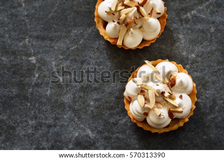 Tartlet with meringue and almonds on a concrete background
