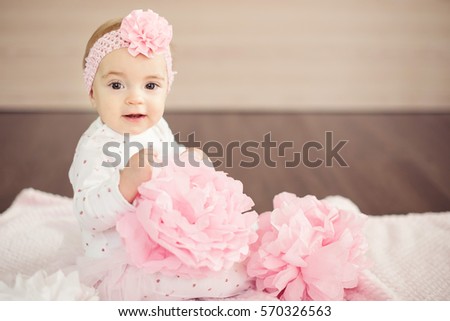 A baby girl in a pink flower headband with paper flowers in her hands. Charming baby.