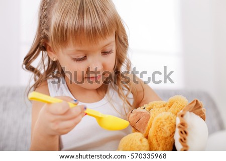 Cute blonde little girl feeding her teddy bear.