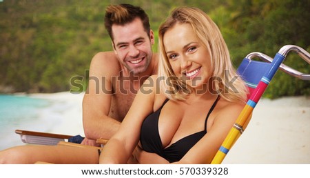 Happy good looking millennial couple sitting at the beach smiling at camera