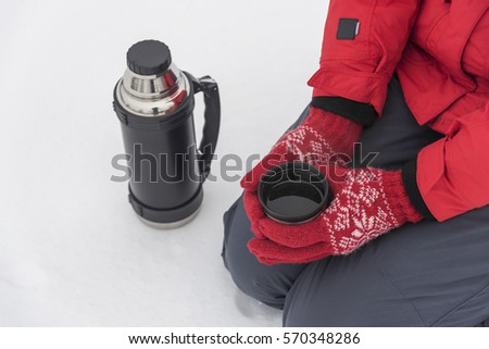 Women's hands are holding a thermos on a background of a winter landscape.