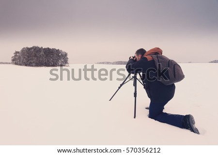 Photographer taking a picture. Man with camera on snow make landscape photo. Photographer on snowy background.