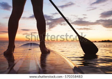 paddle board on the beach, close up of standing legs and paddle Royalty-Free Stock Photo #570358483