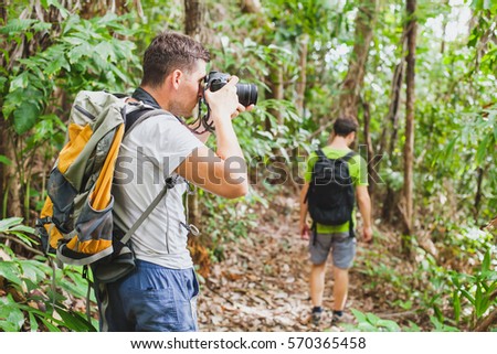 nature travel photographer in tropical jungle, group of tourists hiking in the forest, man taking photo with big camera