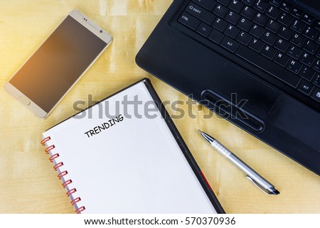 A blank book with text trending, smartphone and laptop.