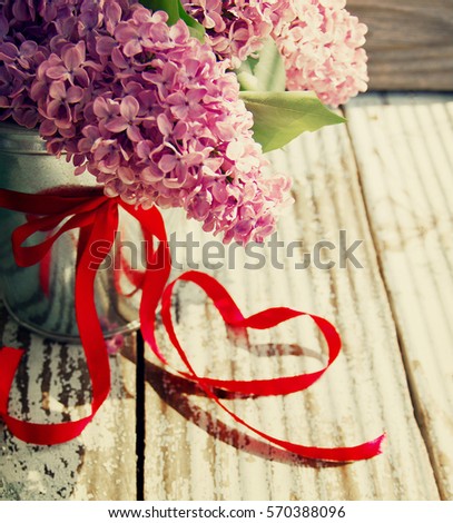 Lilac bouquet in the metal bucket decorated with a red tape and a bow on a wooden surface in vintage style. Romantic bouquet of a lilac
