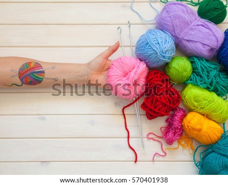 A woman with a tattoo in the form of a ball of wool keeps the skein. Background of white wood.
