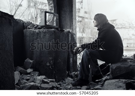 Homeless man watching broken TV-set in the ruined interior. Shallow depth of field due to the tilt lens for movie effect Royalty-Free Stock Photo #57045205