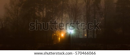 The house in winter forest at night in the fog, lantern light, trees without leaves