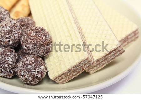 Various confectionery on plate, chocolate balls, wafer witch chocolate layers and cookies on white background