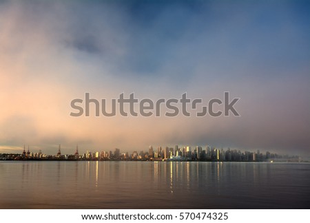 Distant city skyline shining in the early rays of sun with fog and reflection in a body of water