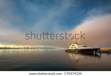 Distant city skyline shining in the early rays of sun with fog and reflection in a body of water and a large yacht 