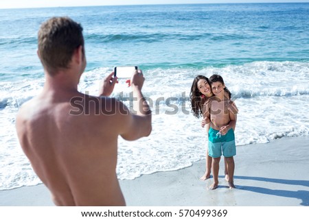 Father photographing happy wife and son at sea shore