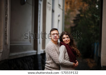 Young couple wearing on tied warm sweaters hugging in love under arch at city in autumn.