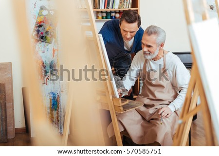 Handsome artist helping elderly man in painting