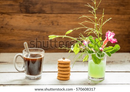 Black coffee, cookies and flower vase on wood background