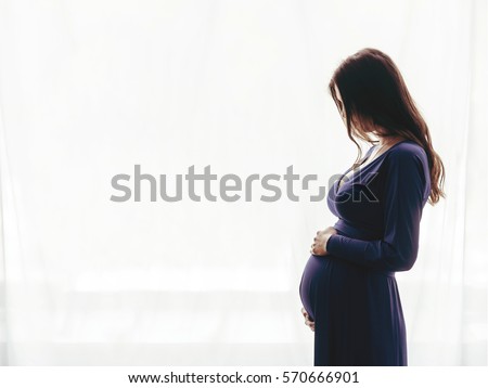 Pregnant woman standing against the window Royalty-Free Stock Photo #570666901