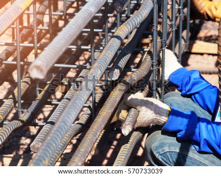 workers hands using steel wire and pincers to secure rebar before concrete is poured over it.